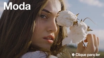Uma mulher com cabelos castanhos longos segura uma planta de algodão perto do rosto. O texto na imagem diz: “Moda”