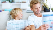Cute happy kid looking at dad while dad reads news paper  Cute happy kid looking at dad while dad reads news paper