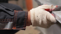 A worker wearing white gloves and a dark jacket installing a metal strip.