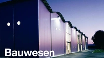 Eine moderne Gebäudeaußenansicht in der Dämmerung mit eingeschalteter Beleuchtung. Der Text auf dem Bild lautet: „Bauwesen.“