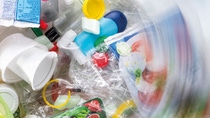 Vue aérienne d’une masse de déchets plastiques colorés comprenant des emballages alimentaires, des gobelets et des bouteilles jetables - les bords de l’image sont flous pour donner l’impression que les déchets tournent en rond. 
