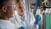 A man and a woman wearing protective goggles stand in a laboratory. A man and a woman wearing protective goggles stand in a laboratory.
