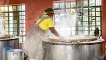 A woman stands in front of a huge vat of rice and stirs it.