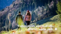 Un homme et une femme traversent une prairie de montagne par une journée ensoleillée. Ils portent des vêtements chauds d’extérieur.
