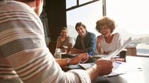 Shot of mixed race young people sitting at a table discussing new and creative business ideas. Smiling african woman sitting with colleagues in a meeting.