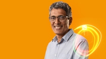 A BASF employee stands against an orange background, smiling at the camera, with glowing light trails in front of him.