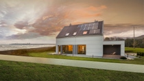 Stormy dark clouds gather over a white modern house with a small green lawn and solar roof panels located next to a beach with the rough waves just a few meters away. Stormy dark clouds gather over a white modern house with a small green lawn and solar roof panels located next to a beach with the rough waves just a few meters away.
