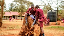 Two boys sit on a tree stump and eat lunch.