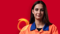 A BASF employee in an orange work jacket stands against a red background, looking at the camera, with glowing light trails beside her.