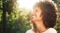 Close up portrait of a beautiful confident woman with dark, curly hair laughing in the sunshine with green trees in the background. Close up portrait of a beautiful confident woman with dark, curly hair laughing in the sunshine with green trees in the background.