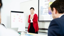 A BASF employee stands in front of a flipchart and presentation screen, smiling while leading a meeting, with colleagues listening in the foreground.