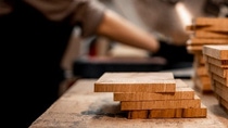 Wooden boards lying on a table. In the background a man is working with the wooden boards.