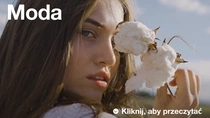 Kobieta o długich brązowych włosach trzyma roślinę bawełny blisko twarzy. Tekst na zdjęciu brzmi: „Moda”