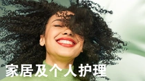 一个微笑的黑色卷发女性。图像上的文字为“家居与个人护理”。 