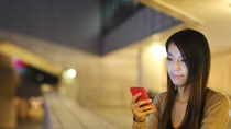 Woman standing at a train station looking at her phone with red phone cover 