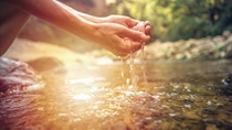 Human hand cupped to catch the fresh water from the river, reflection on water surface.