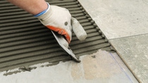 Laying Ceramic Tiles. Troweling mortar onto a concrete floor in preparation for laying white floor tile.