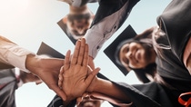 Students, graduation and group with hands stacked for college celebration outdoor. Below diversity men and women together for university achievement, education success and school graduate event.