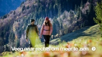 Een man en vrouw lopen over een bergweide, op een zonnige dag. Ze dragen warme buitenkleding. Een man en vrouw lopen over een bergweide, op een zonnige dag. Ze dragen warme buitenkleding.