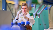 A woman in a lab stirring a liquid in a beaker.