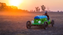 A man sitting in an electric vehicle on a field by sunset. A man sitting in an electric vehicle on a field by sunset.