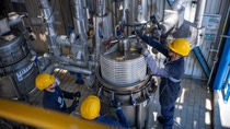 Industrial workers wearing protective helmets and workwear operate and secure heavy equipment inside a chemical processing facility.