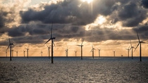 Der Windpark „Oersted“ in der deutschen Nordsee bei Sonnenuntergang, große graue Wolken verdecken die Sonne vor einem orangefarbenen Himmel. Der Windpark „Oersted“ in der deutschen Nordsee bei Sonnenuntergang, große graue Wolken verdecken die Sonne vor einem orangefarbenen Himmel.