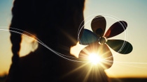 A silhouette image of a child with a rainbow coloured pinwheel, looking at the sunset setting on the horizon, with sketch lines showing the path of the wind over her pinwheel. A silhouette image of a child with a rainbow coloured pinwheel, looking at the sunset setting on the horizon, with sketch lines showing the path of the wind over her pinwheel.