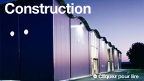 Un bâtiment moderne à l’extérieur au crépuscule avec des lumières allumées.  Le texte de l'image indique : « Construction » 
