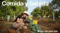 Una agricultora, con mono y sombrero, sostiene una tableta y examina las plantas en un campo en un día soleado. En el texto de la imagen pone: “Alimentos y bebidas”.