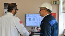 A man and a woman in work clothes operate a factory machine.