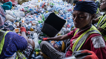 Three people sorting through a large pile of plastic bottles.