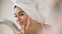 Woman with hair in towel rubbing lotion on face
