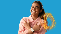 A smiling BASF employee in a pink shirt stands against a blue background, crossing her arms and pointing to the side, with glowing light trails. 
