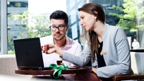 Ein Mann und eine Frau im Anzug schauen gemeinsam auf einen Laptopbildschirm Ein Mann und eine Frau im Anzug schauen gemeinsam auf einen Laptopbildschirm