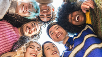 A diverse group of people stand close together in a circle, looking down at the camera.