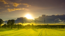 A row of wind turbines stand in a country field against a partly cloudy sky with the sun setting behind the clouds. A row of wind turbines stand in a country field against a partly cloudy sky with the sun setting behind the clouds.