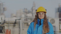 An engineer wearing a hard hat and safety goggles stands in front of an industrial plant.