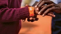 Im Fokus stehen zwei Hände. Um einem Arm ist ein Tap2Eat-Armband umgelegt.