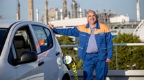 A men in a blue BASF uniform standing next to a white electric vehicle. 
