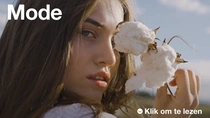 Een vrouw met lang bruin haar houdt een katoenplant dicht bij haar gezicht. De tekst op de afbeelding luidt: "Mode".