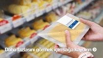 Bir kişi, markette dilimlenmiş peynir içeren plastik bir paketi tutuyor. Arka planda çeşitli peynir türleriyle dolu raflar görülüyor. 
