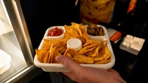 Hand holding a white compostable food tray with tortilla chips, salsa dip, and snacks at a food stand. Hand holding a white compostable food tray with tortilla chips, salsa dip, and snacks at a food stand.