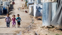 Three children holding hands walking down a dirt road 