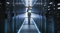 IT Technician Works on Laptop in Big Data Center full of Rack Servers. He Runs Diagnostics and Maintenance, Sets System Up. IT Technician Works on Laptop in Big Data Center full of Rack Servers. He Runs Diagnostics and Maintenance, Sets System Up.
