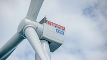 Eine Windturbine wird zusammengebaut und ein Kran auf einer Plattform im Meer hebt die Turbinenblätter nach oben. Eine Windturbine wird zusammengebaut und ein Kran auf einer Plattform im Meer hebt die Turbinenblätter nach oben.