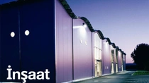 Alacakaranlıkta ışıklar açık modern bir bina dış cephesi.&nbsp; Resimdeki metinde şunlar yazıyor: "İnşaat"