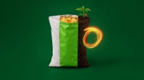 Packaging bag transitioning from plastic pellets to soil with a sprouting tomato plant, against a green background. An orange light swirl appears on the right side of the bag.