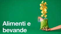 Una agricoltrice, con indosso una salopette e un cappello, tiene in mano un tablet mentre osserva le piante in un campo in una giornata di sole. Il testo sull’immagine recita: “Cibi e bevande”. 