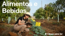 Uma agricultora, vestindo macacão e chapéu, segura um tablet e examina plantas em um campo em um dia ensolarado. O texto na imagem diz: “Alimentos e bebidas”. Uma agricultora, vestindo macacão e chapéu, segura um tablet e examina plantas em um campo em um dia ensolarado. O texto na imagem diz: “Alimentos e bebidas”.